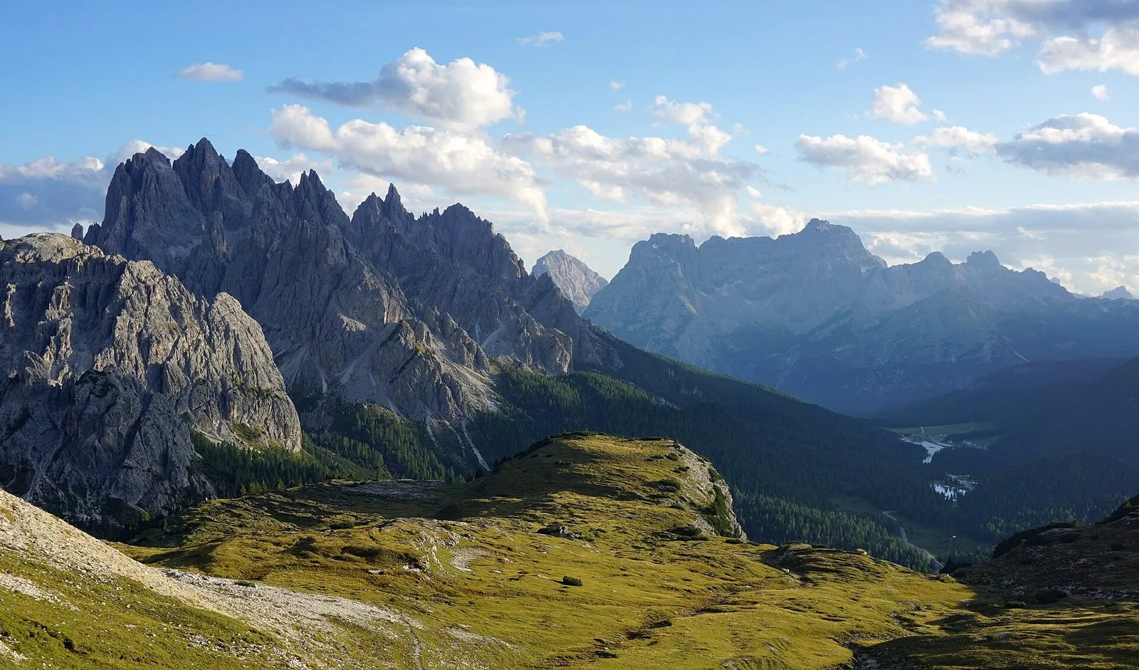 Le guglie frastagliate dei Cadini di Misurina a sinistra, pascoli d'alta quota in primo piano e la valle di Misurina con il lago sulla destra