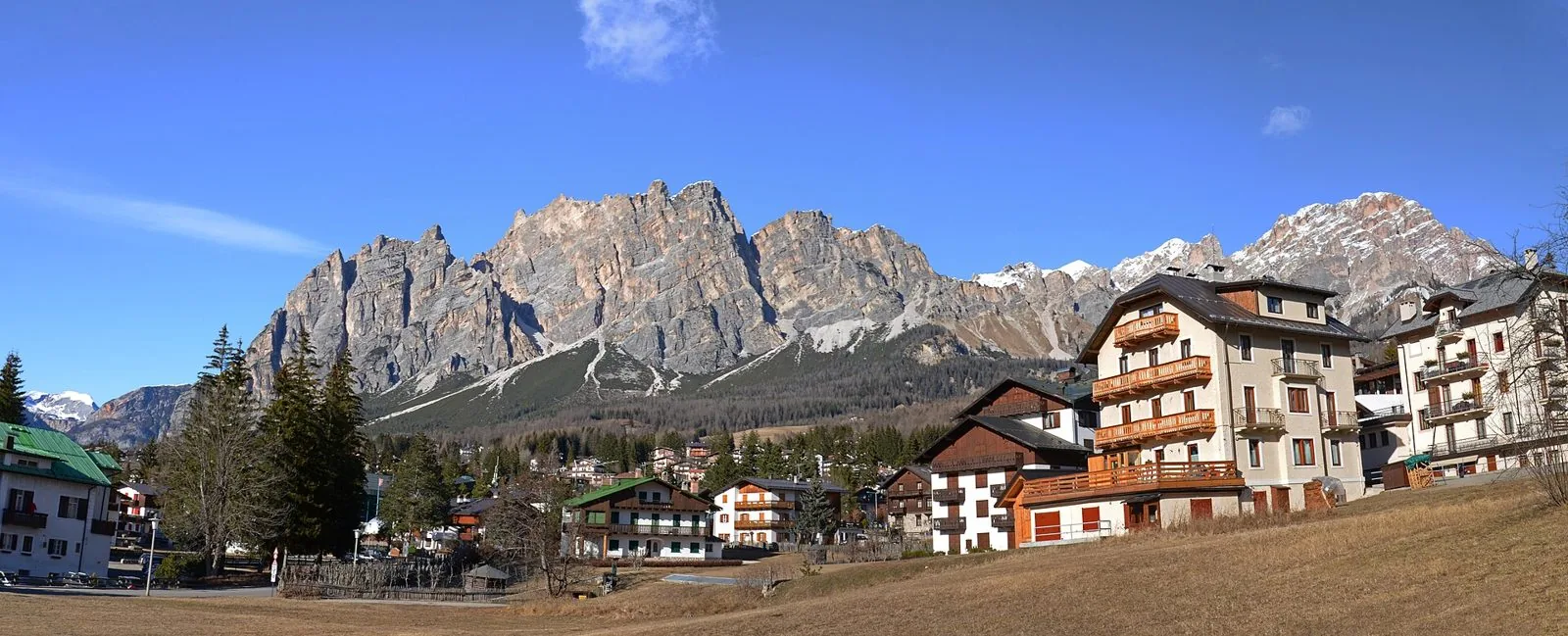 Case e palazzine in stile alpino di Cortina d'Ampezzo con balconi in legno, sotto le pareti rocciose del Pomagagnon e le cime innevate in lontananza