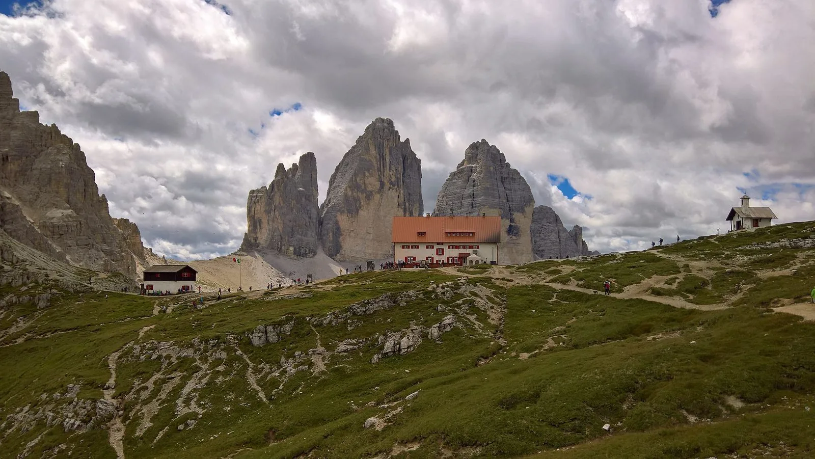 Le pareti nord delle Tre Cime di Lavaredo dietro il Rifugio Locatelli, con la piccola cappella sulla destra e prati d'alta quota in primo piano