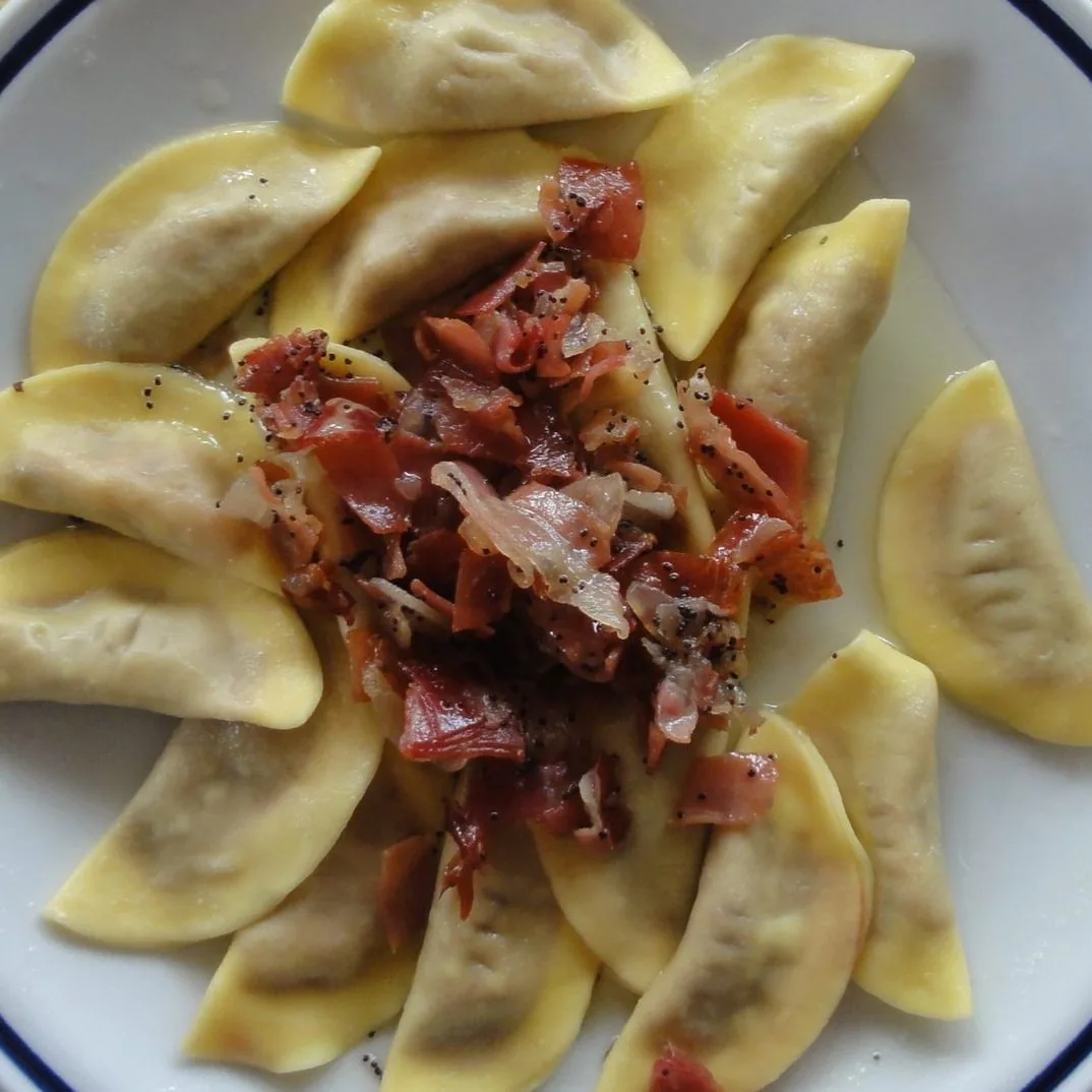 Piatto di casunziei a mezzaluna conditi con burro, semi di papavero e pezzetti di speck croccante